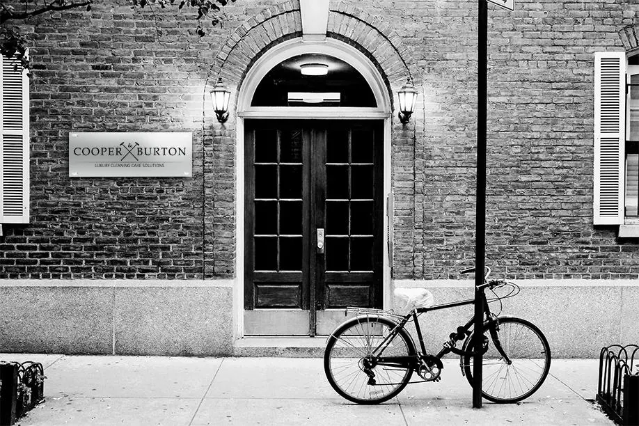 Schwarz-Weiß-Fassade mit Eingangstür und Schild COOPER & BURTON, Fahrrad davor